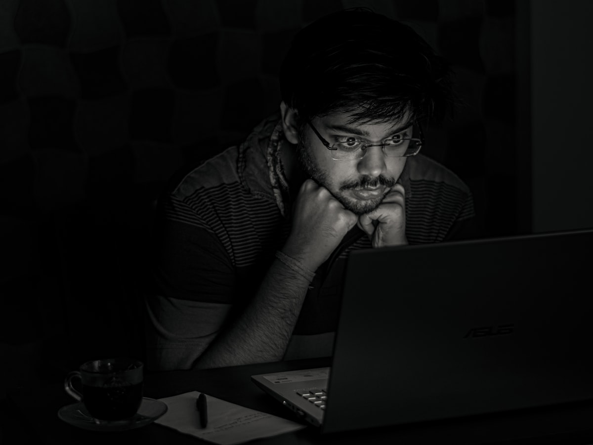 어두운 방 안에서 모니터 세 대를 띄워두고 데이터 차트와 영문 텍스트가 가득한 이력서를 분석하며 미간을 찌푸린 채 집중하는 개발자의 뒷모습